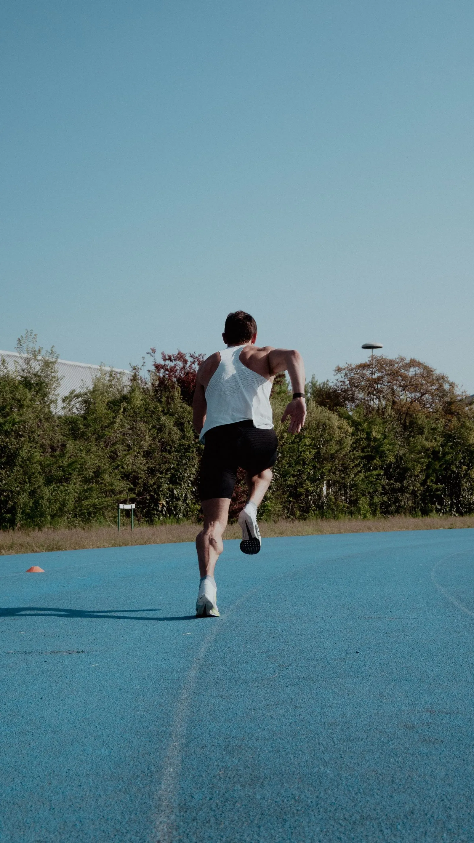 Løper sett bakfra som sprinter på en blå løpebane